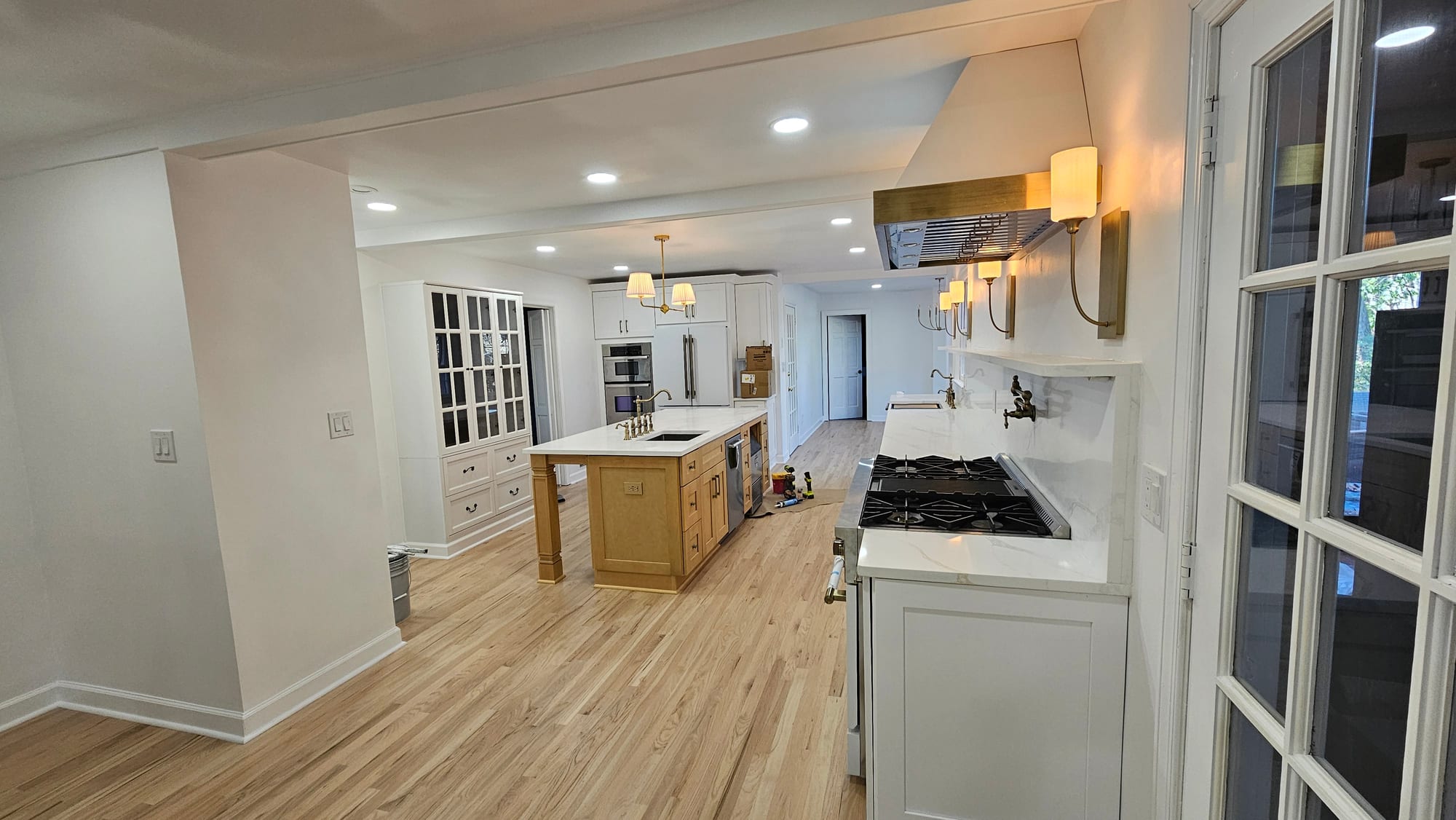 Renovated kitchen with a built-in glass-front china cabinet, brass range hood, and French door