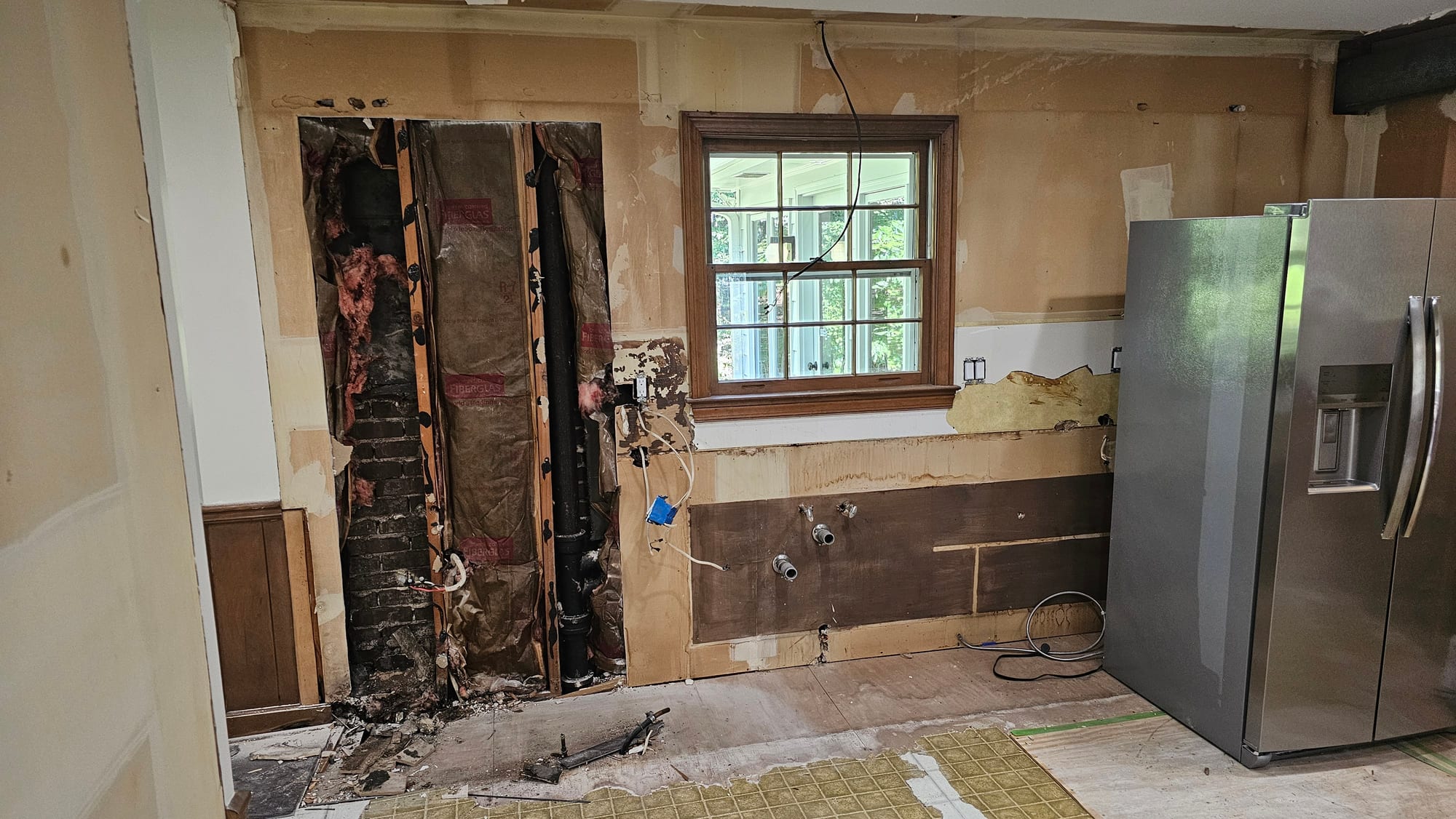 Kitchen wall opened to the brick chimney chase, with a window and plumbing rough-in, during demolition
