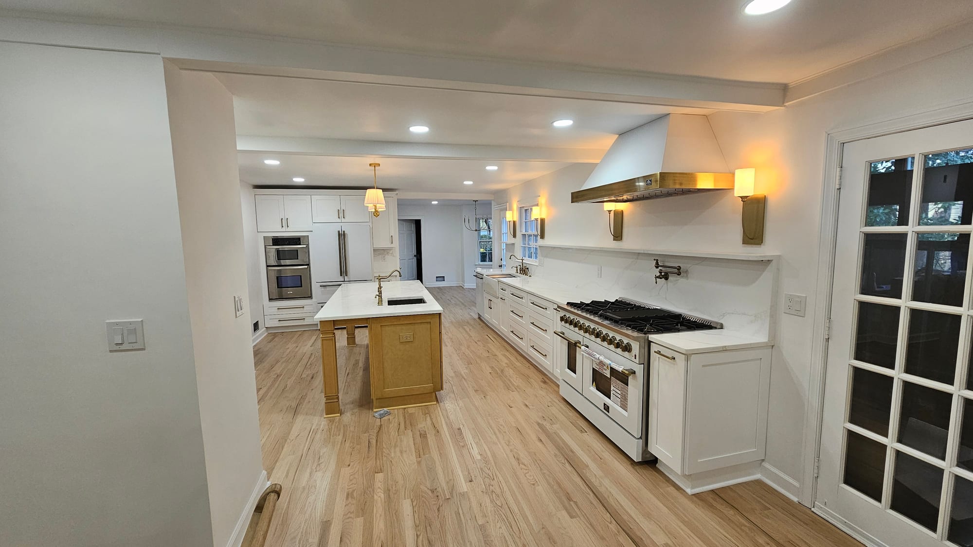 Renovated kitchen showing the full cabinet run toward the dining area, with range and brass hood