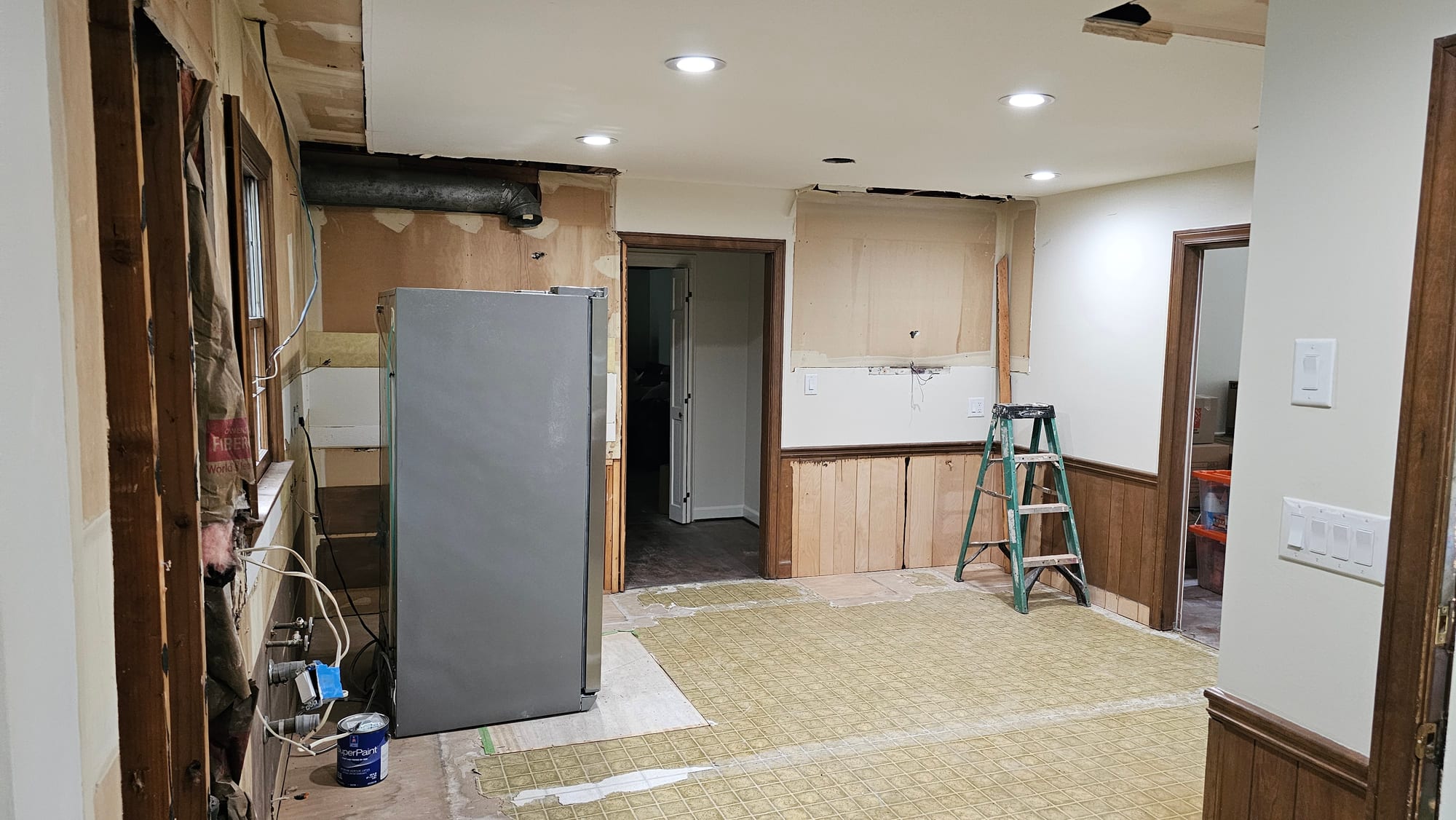 Kitchen gutted to subfloor with a refrigerator and ladder, under construction