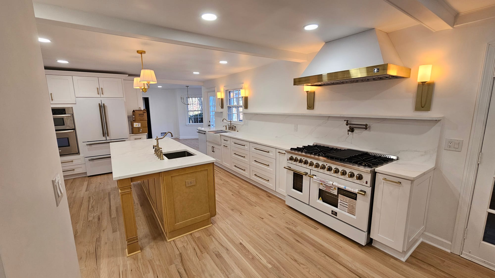 Renovated kitchen island with the refrigerator wall and brass range hood beyond