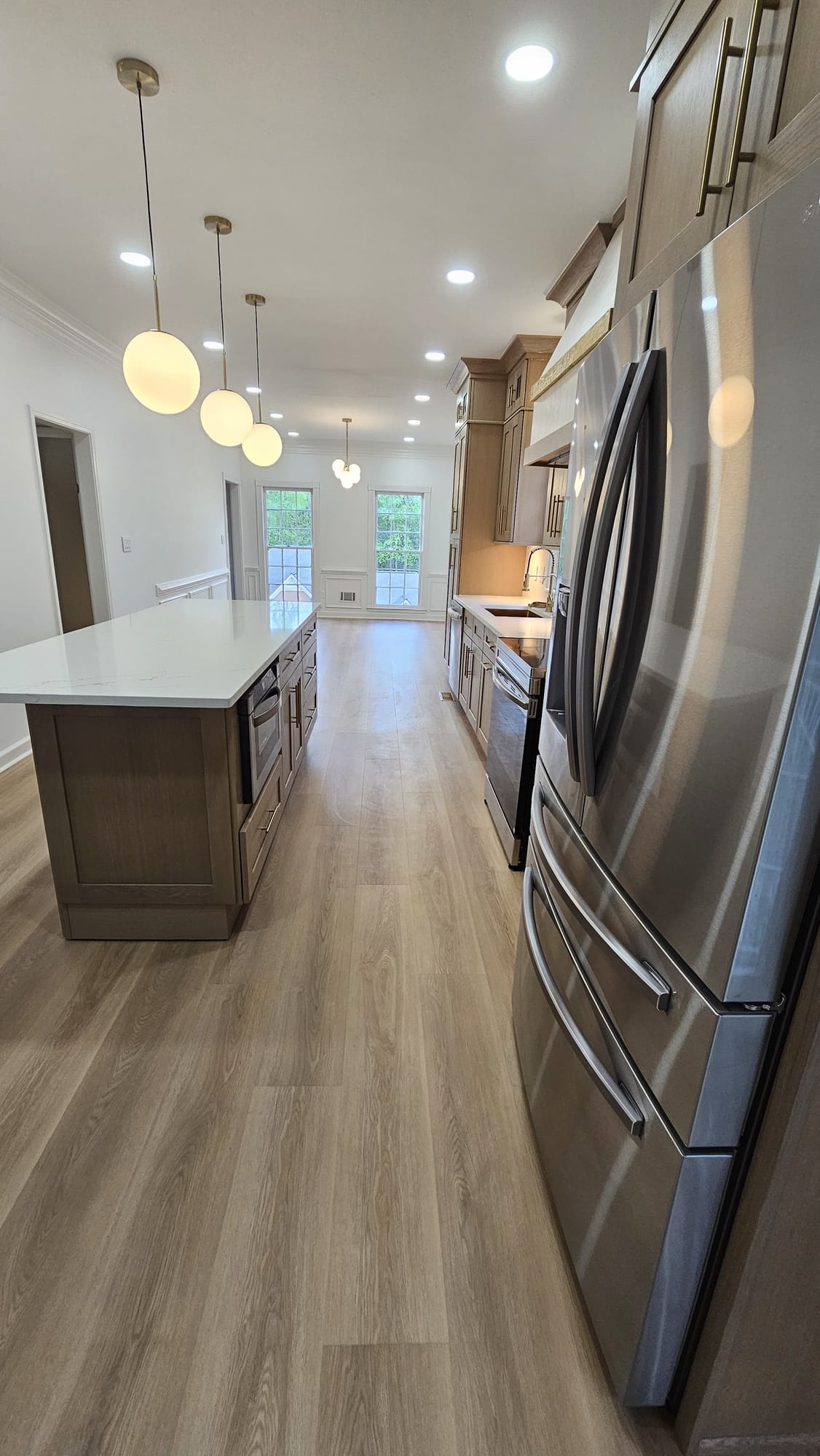 Renovated kitchen island beneath globe pendant lighting with wood cabinetry and a stainless refrigerator