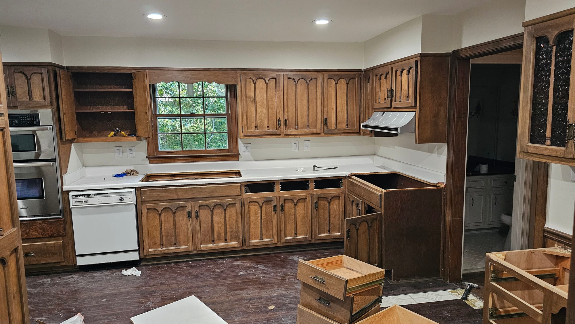 Kitchen with oak arched-panel cabinets, a dishwasher, and a window over the counter, before renovation