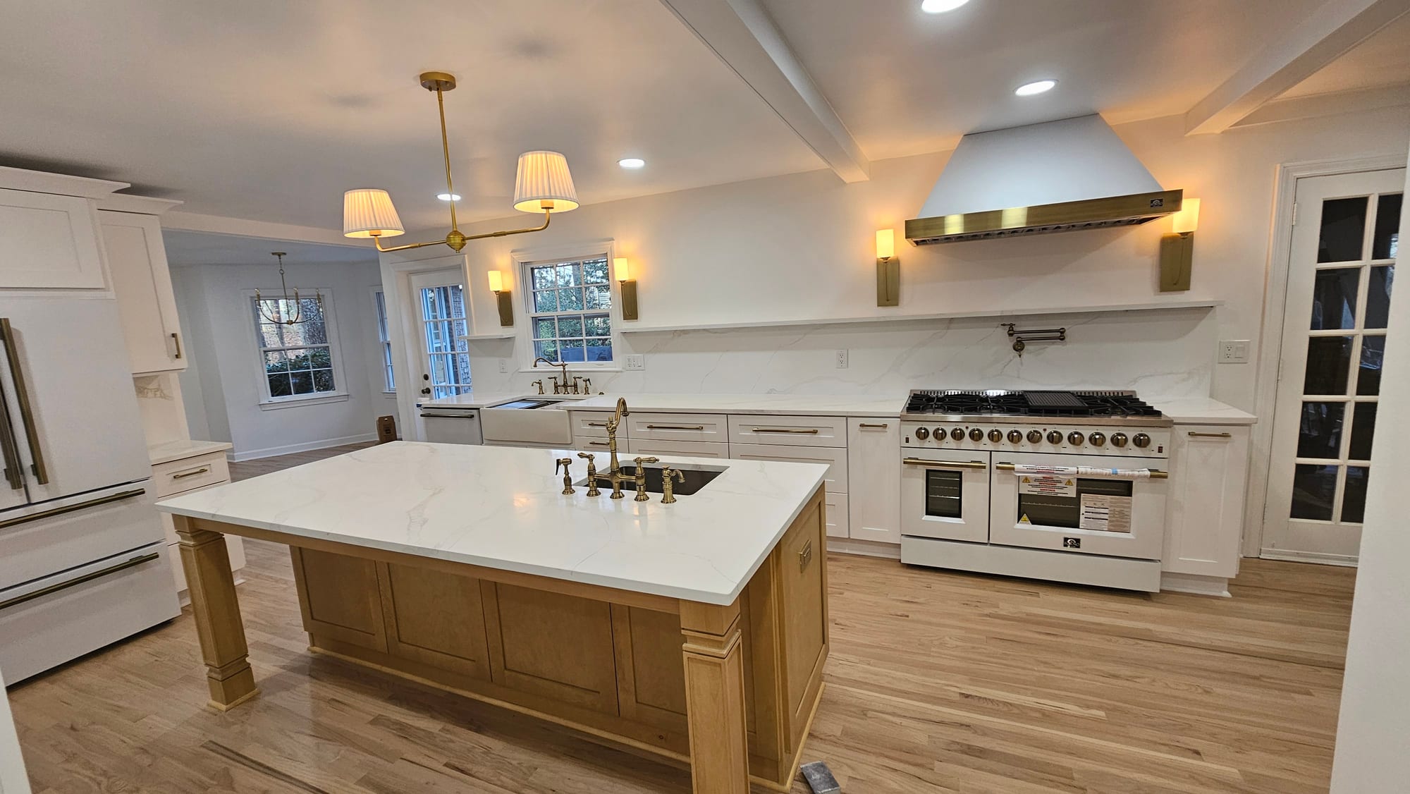 Renovated kitchen with white shaker cabinetry, a brass range hood, and a paneled refrigerator on the same wall