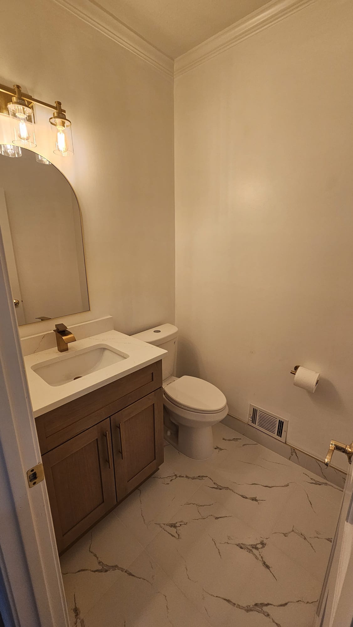 Powder room with a wood vanity and arched mirror