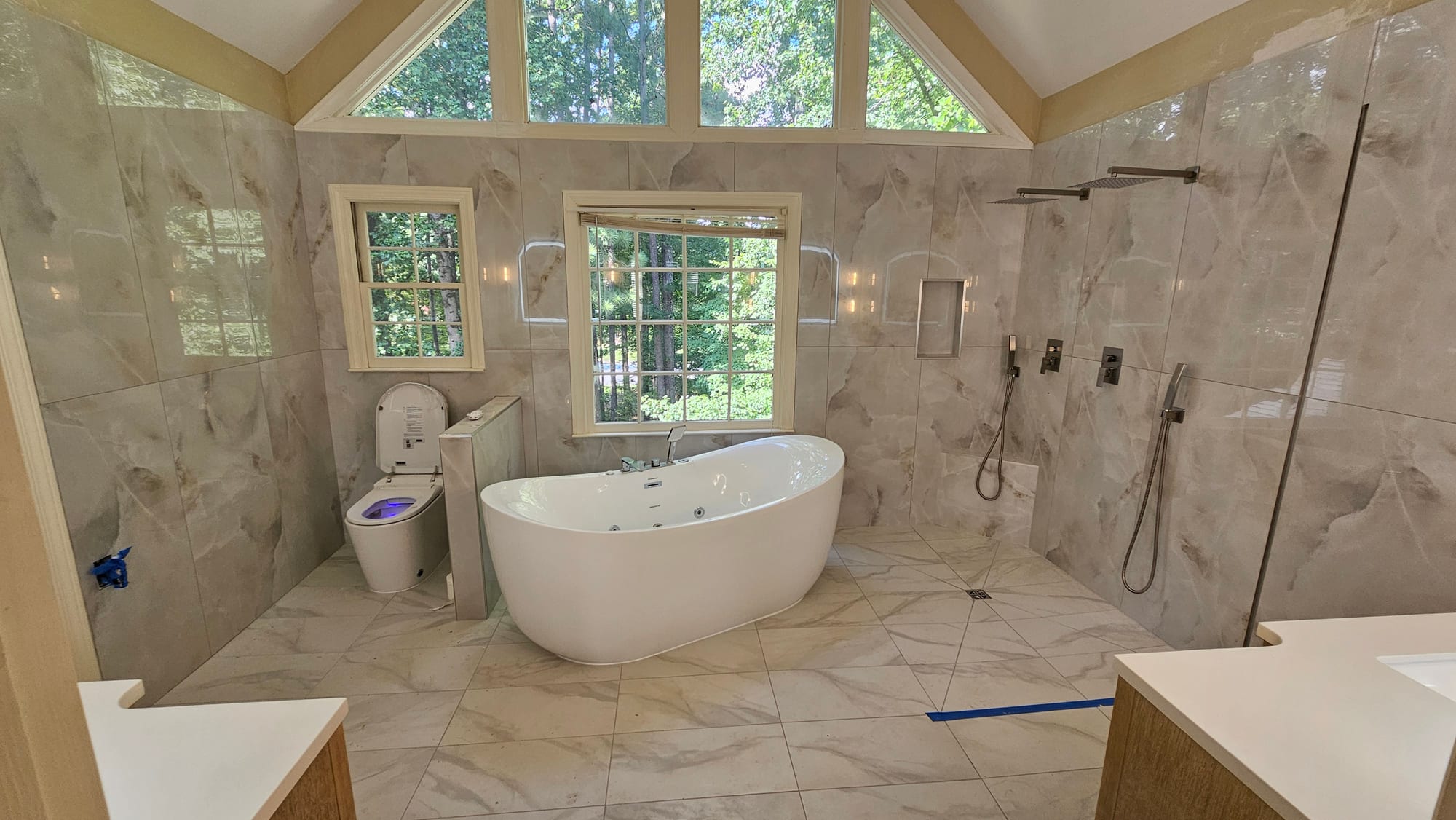 Primary bathroom with a freestanding soaking tub beneath a cathedral window, marble tile, and an open shower