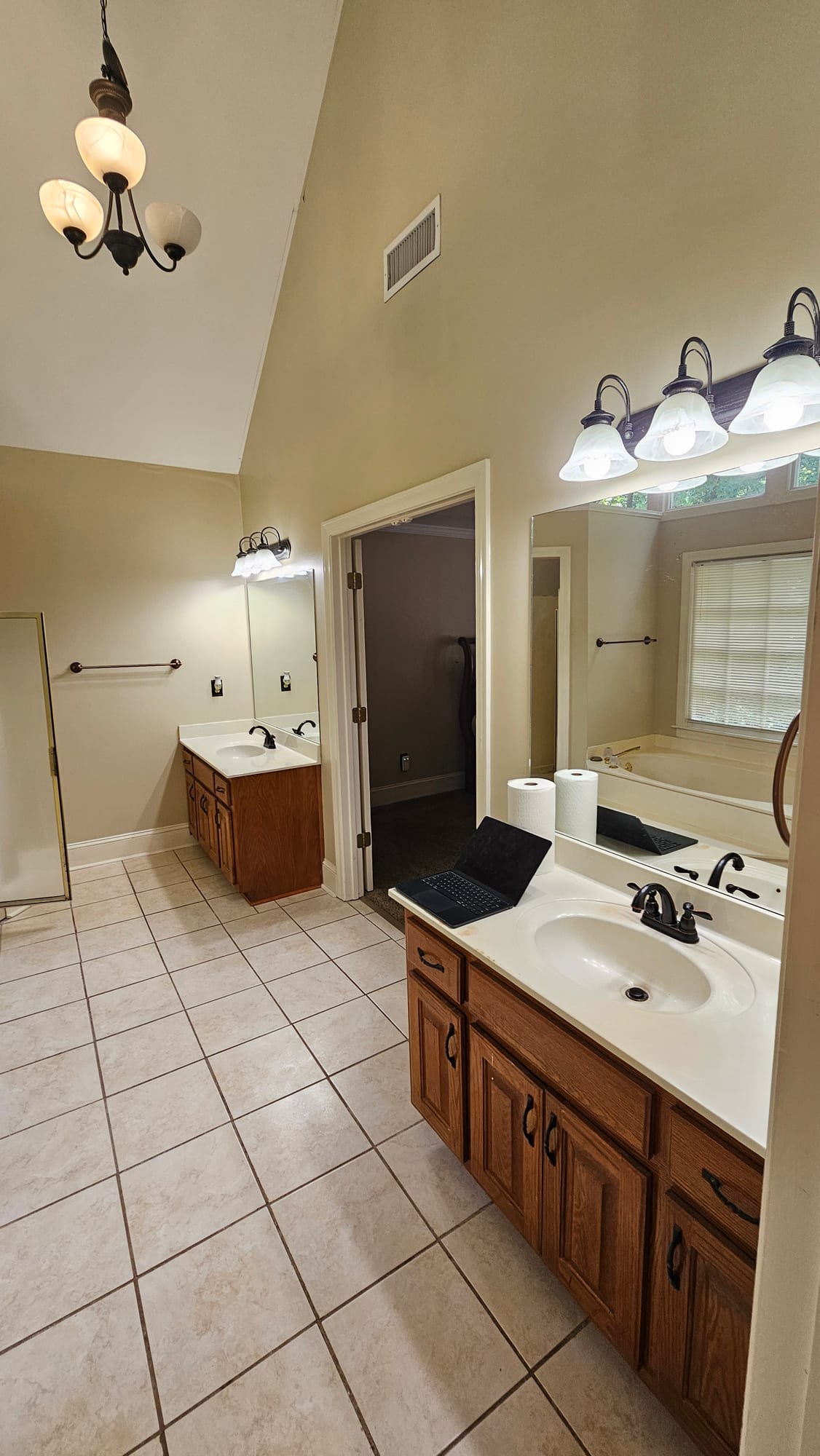 Primary bathroom with an oak double vanity beneath an arched window, before renovation