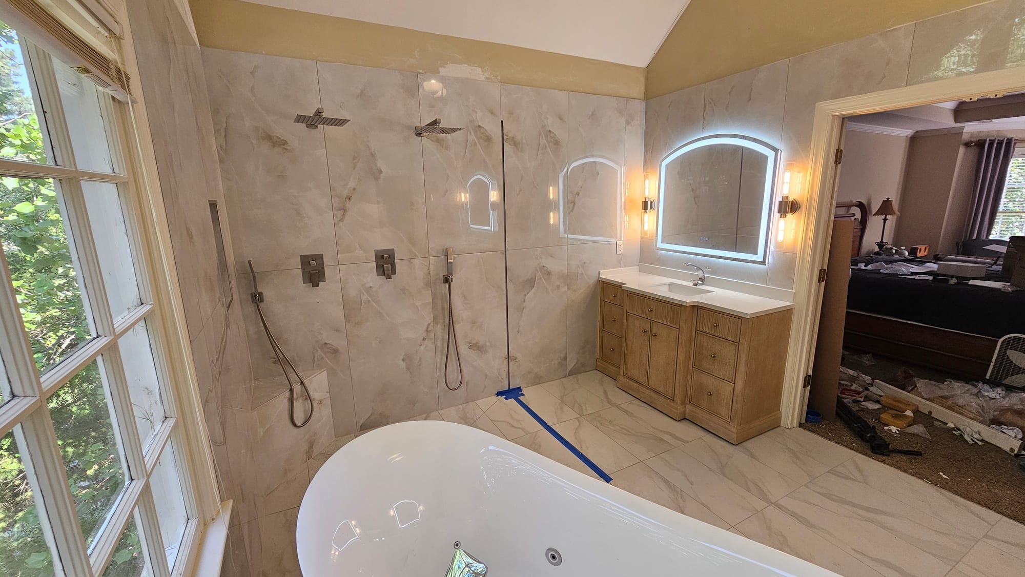Primary bathroom with a wood double vanity, backlit arched mirror, and a doorway to the bedroom