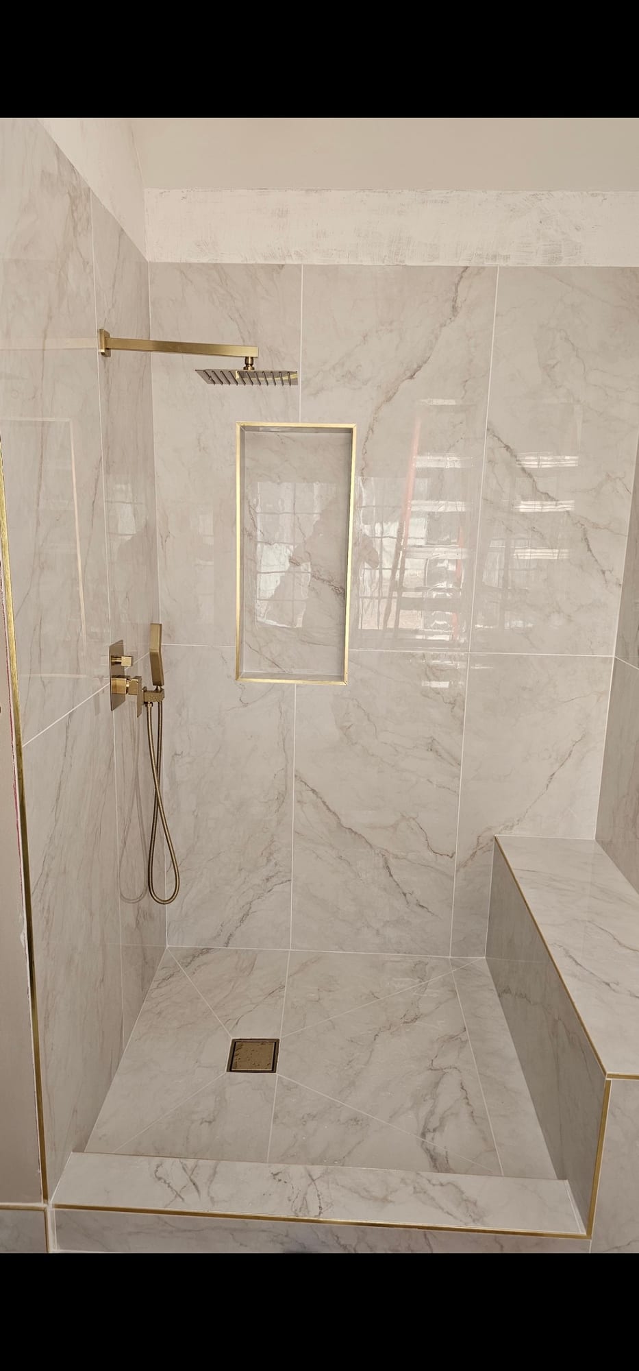 Marble shower with gold trim and a bench seat, under construction